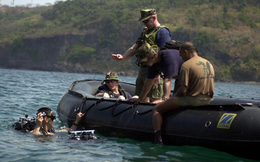 A Navy diver holds on to the Zodiac and gets instruction from fellow Underwater Construction Team TWO members while a Filipino service member checks his gear before they dive to 20 feet.