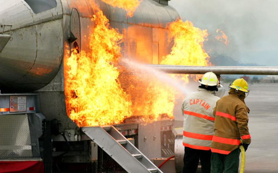 Ron Hall, Naval Air Station (NAS) Sigonella Fire Department battalion chief, and Aviation Boatswain&#39;s Mate 1st Class Stephen Mark, NAS Sigonella Fire Department assistant training officer, spray water on a fire coming from a Mobile Aircraft Fire Trainer (MAFT) on the NAS Sigonella flightline.