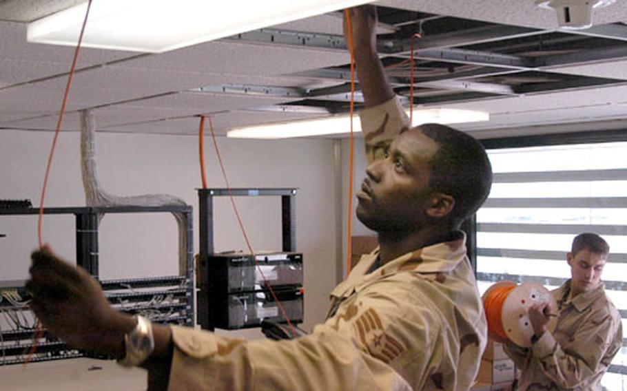 Staff Sgt. Shawn German runs wire along a ceiling at Baghdad International Airport, as Senior Airman Matthew Davidson holds the cable drum. German, Davidson and other members of the 447th Expeditionary Communications Squadron stationed at the airport are helping rewire the civilian terminal's outdated and overloaded communications lines.