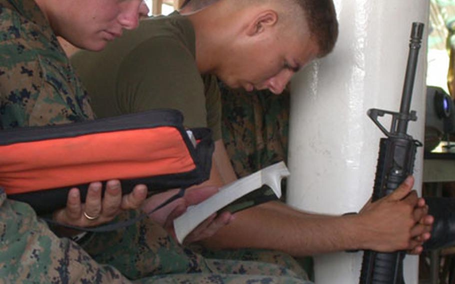 Sgt. Mike Haddle, 24, center, reads a Bible while Cpl. Osmar Araujo, 22, right, bows his head in prayer before Easter Sunday service held in the pavilion at the headquarters base for 3rd Battalion, 8th Marines in Port-au-Prince, Haiti.