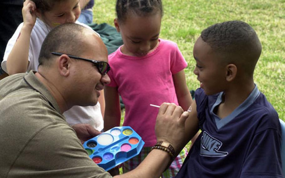 Matthew Welch (right), age 8, gets a tattoo painted on at the Third Annual Children’s Health and Safety Fair at Camp Zama by (left) Miki Nihipali, while Nicole Welch (center), Matthew's sister, watches.