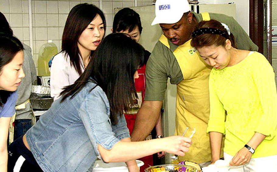 Marvin Sanders, center, walks a group of new brides through the cooking portion of the USO's Cross-Cultural School at Camp Kim, South Korea.