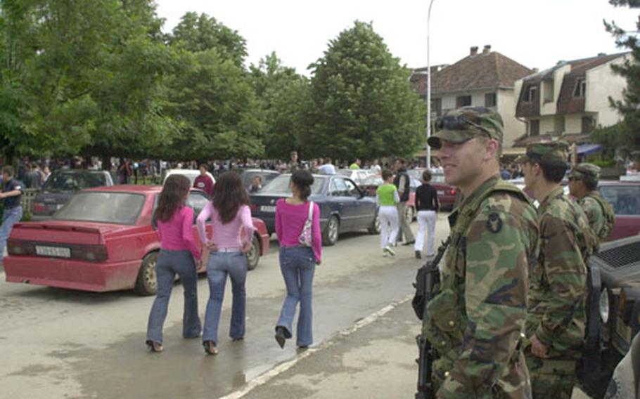 Spc. Matthew Vander Plas, translator Bleirm Bela and Spc. Gamaliel Ibarra watch the procession of young Kosovars along the main street of Vitina during a patrol Monday. The Minnesota National Guardsmen have responsibility for the city and visit it routinely to make sure nothing's wrong. They soon had a lot of company, with some sunshine and a high school graduation combining to put hundreds of young people on the street.