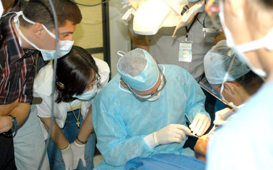 Iraqi dentists from the University of Baghdad Dental School watch Lt. Col. Robert Herold, center, a periodontist with the 31st Combat Support Hospital in Baghdad, peform a tooth extraction on Spc. Lahendra McCray Tuesday. Assisting is Spc. Alicia Hernandez, right.