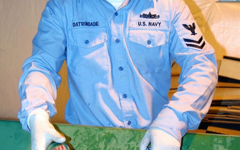 Petty Officer 2nd Class Alexander Datrindade ensures cans are steadily input into the Atsugi Naval Air Facility Recycling Center's aluminum crusher.