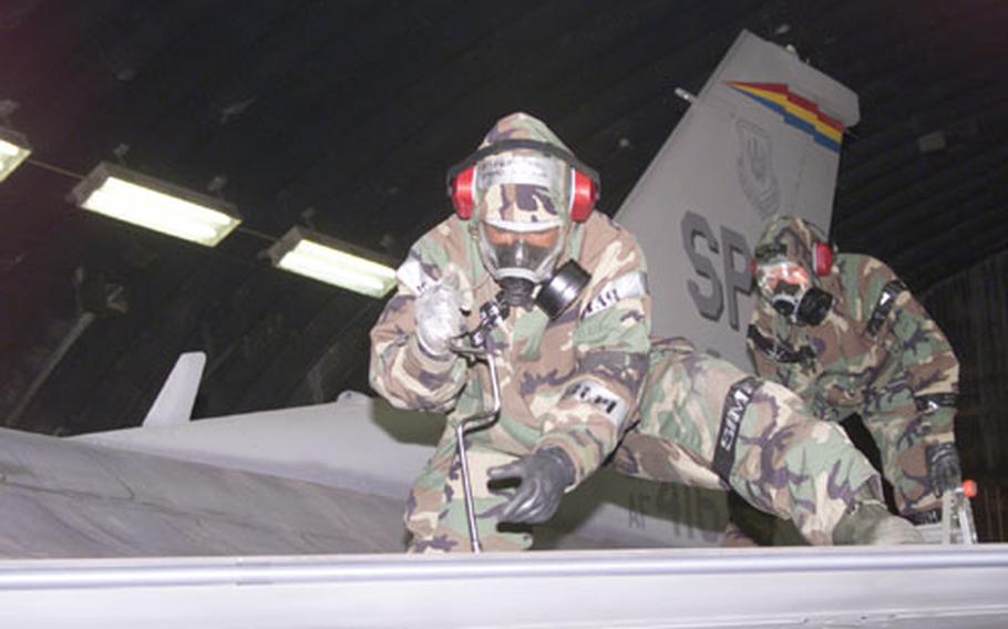 Airmen 1st Class Philip Behneke, foreground, and Jared Cripe, 52nd Aircraft Maintenance Squadron avionics technicians, wear full chemical warfare gear while making last-minute checks on an F-16CJ aircraft prior to launch Monday, as part of a NATO tactical evaluation.