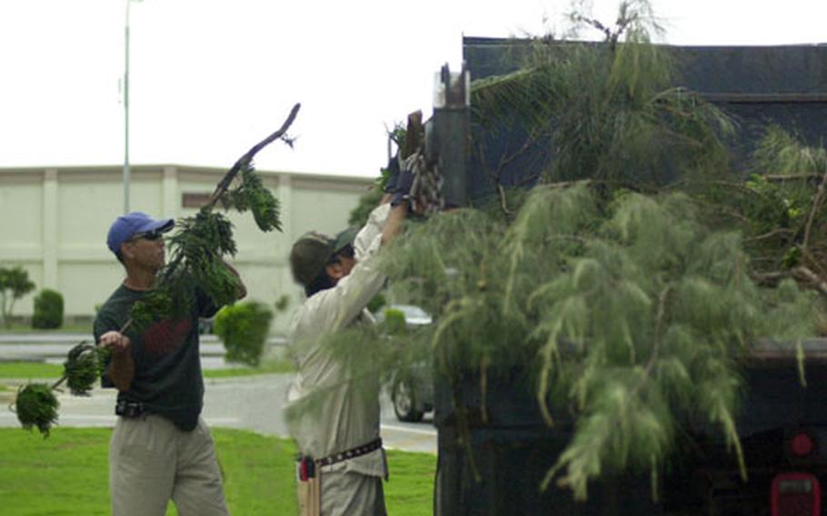 Atsushi Matayoshi (left) and Toru Gima from Kadena’s 18th Civil Engineer Squadron hurl broken tree branches and similar debris into a dump truck Wednesday morning at O’Connor fitness center on Kadena Air Base. The branches were ripped off by Tropical Storm Megi.