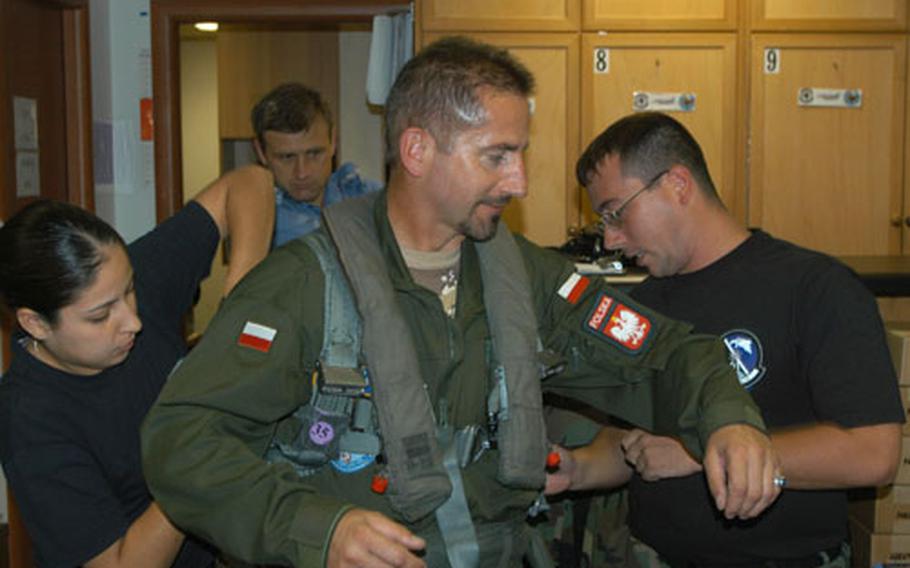 Airmen 1st Class Vanessa Hermosillo and Donald Morell adjust part of Polish air force Col. Wladyslaw Lesnikowski's flight suit Monday during the first day of a visit to Aviano Air Base, Italy. Aviano is showing more than a dozen officers from Poland, which is buying 48 F-16 jets, how the Air Force operates and maintains its fleet.