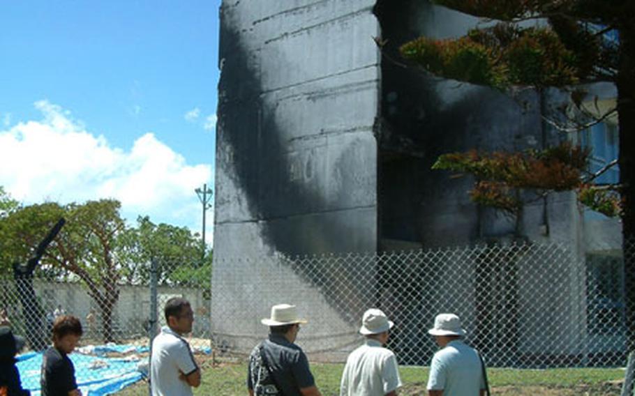 Participants in Sunday's rally at Okinawa International Univerity stop by the school's Administration building to view the blackened end where a helicopter clipped the building and crashed, bursting into flames. More than 30,000 people attended the rally, said Ginowan city officials, who hosted the event.