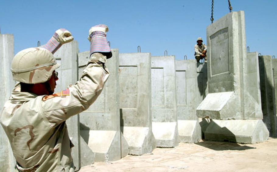 Spc. Matthew Fox, left, signals to move a concrete barrier after Spc. Sean Stivason hooked the barrier to a crane at Camp Victory, near Baghdad. The two soldiers are from the 458th Engineer Battalion at the camp.