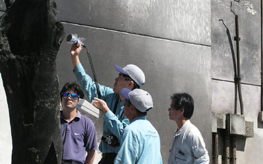 Surveyors with the Japan Analysis Center use a Geiger counter Tuesday to inspect a charred tree stump at the site where a Marine helicopter crashed on the grounds of Okinawa International University Aug. 13. A survey is being made of the area to check for any contamination from the wreckage.