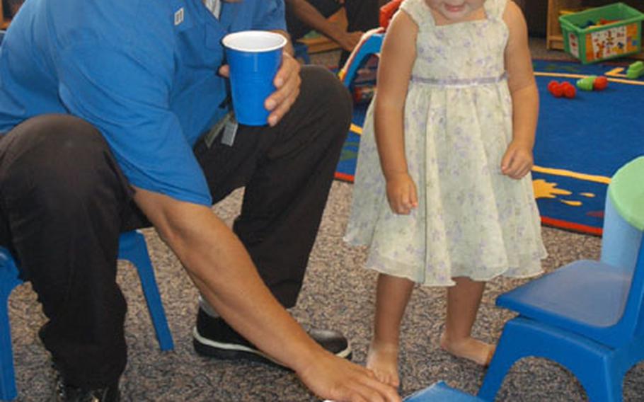 Hospital Corpsman Jamal McCornell plays a song for two-year-old Hanna Goto, daughter of Lt. Cmdr. Mark Goto, at an open house for the U.S. Naval Hospital's new Children's Waiting Room Friday.