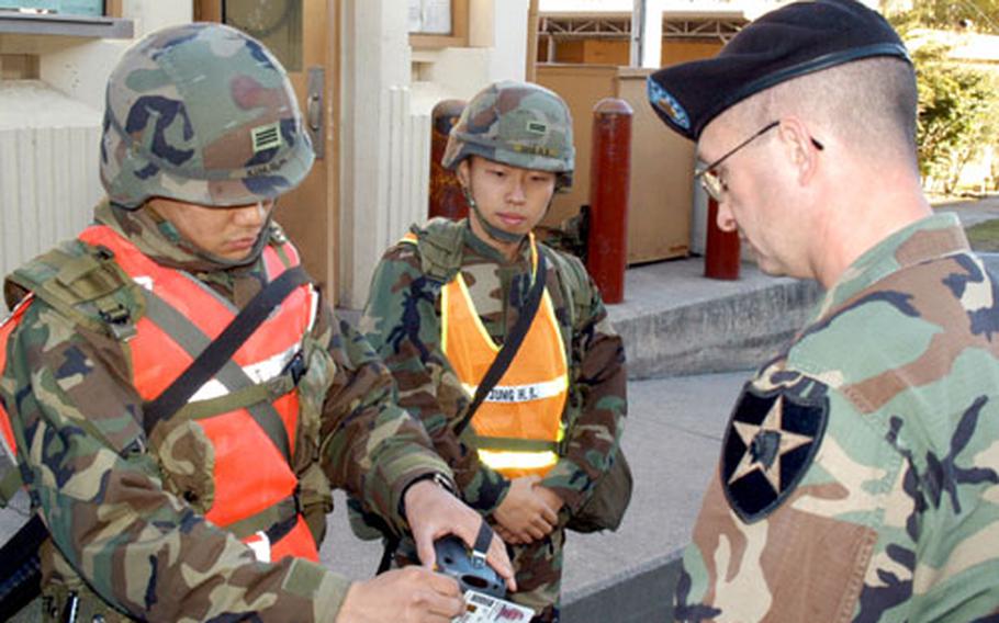 Cpl Kim Simon, left, and Pfc. Jung Hongbae, center, both of the 2nd Infantry Division's Headquarters and Headquarters Company, check 2nd ID spokesman Maj. Mike Lawhorn's identification card at Camp Red Cloud, South Korea, on Thursday.