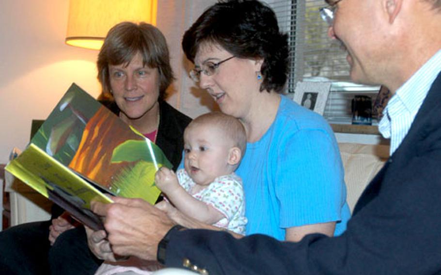 Darmstadt Middle School Principal Dr. Liz Dunham, left, and the elementary school principal, Dr. Russ Claus, watch Pam Landers read to her 8½-month-old daughter, Madeline. Pam Landers was asked to be the honorary chairperson of the new Books for Babies program starting up in Darmstadt’s Department of Defense schools. The book given to Madeline was the first presented under the program.