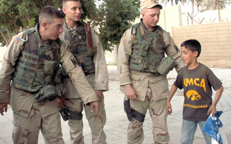 Pfc. Jimmie Frost, Spc. Daniel Buff and Spc. Gary Hiatt with the 89th Military Police Brigade in Baghdad encourage Ahmed, an Iraqi boy who visits with soldiers, to pose like a body builder. Many of the kids in the International Zone wear T-shirts given to them by troops.