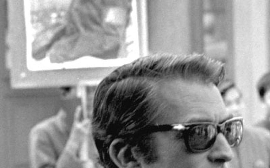 Gregory Peck in front of a banner with a photo of Chairman Mao on it.
