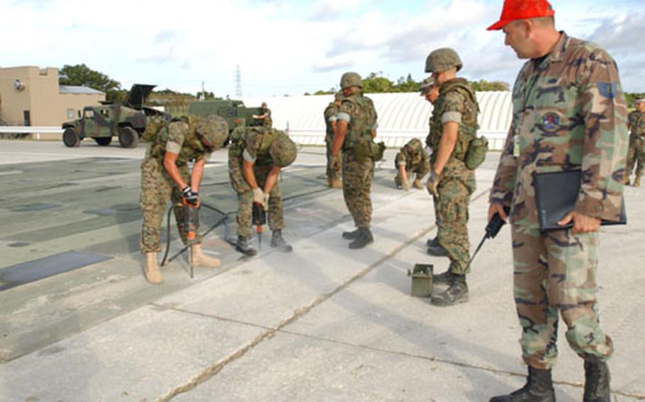 Air Force Tech. Sgt. James Jarvis, right, observes the Marine team to make sure they are drilling anchor holes for the AM-2 matting correctly and safely during an airfield runway repair competition on Kadena Air Base last week. The team from Marine Wing Support Squadron 172 took first place.
