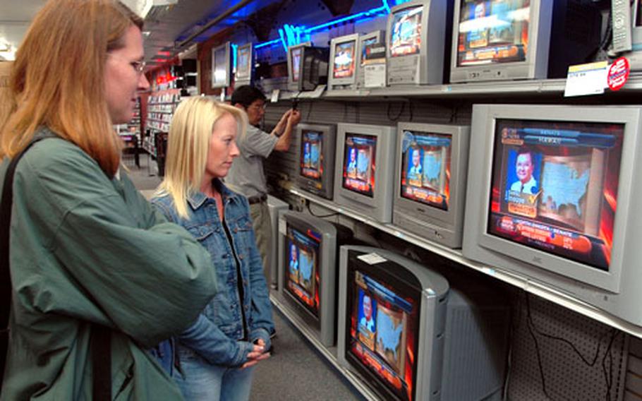 Navy spouses Pamela Correa, left, and Beverley Brinkley interrupt their shopping at the Sasebo Naval Base, Japan, Navy Exchange Wednesday to glance at the various televisions on display, most of them tuned to stations showing election coverage.