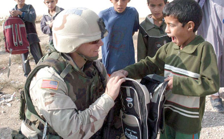 Maj. Brian Grady, with Company B of the 448th Civil Affairs Battalion attached to the 14th Cavalry, 1st Brigade, 25th Infantry Division, shows an Iraqi boy the contents (school supplies) of a backpack.