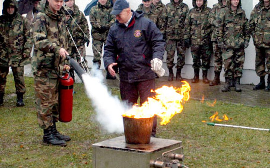 Chief Warrant Officer 3 John Tew, Headquarters and Headquarters Company, Combat Maneuver Training Center, left, puts out a fire with coaching from Hohenfels Fire Department fire inspector Peter Karl Wednesday at Hohenfels. The fire department demonstrated proper use of a fire extinguisher, the danger of putting water on a grease fire and ways to prevent fires in the home.