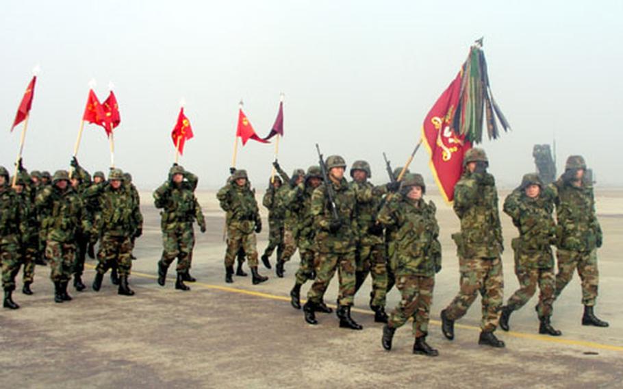 With guidons raised, troops of the Army’s 35th Air Defense Artillery Brigade pass in review at Osan Air Base, South Korea, on Friday morning during a ceremony welcoming them to the 8th U.S. Army. The brigade, newly headquartered at Osan, maintains eight Patriot missile firing batteries at four air bases around the peninsula.