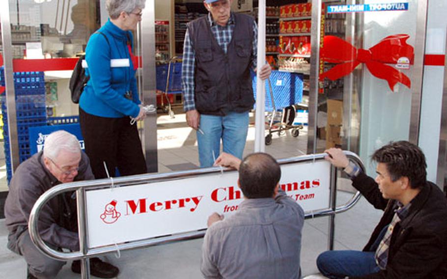 Sasebo Naval Base Navy Exchange General Manager Sandra Franklin, standing at left, and the NEX maintenance department’s Frank Thomas, right, discuss some last minute chores Tuesday before the NEX Auto Mini-Mart’s grand opening Wednesday after a $2.1 million building addition and renovation. Crouching at left is Jim Caron, NEX retail operations manager, helping Japanese workers secure a sign.