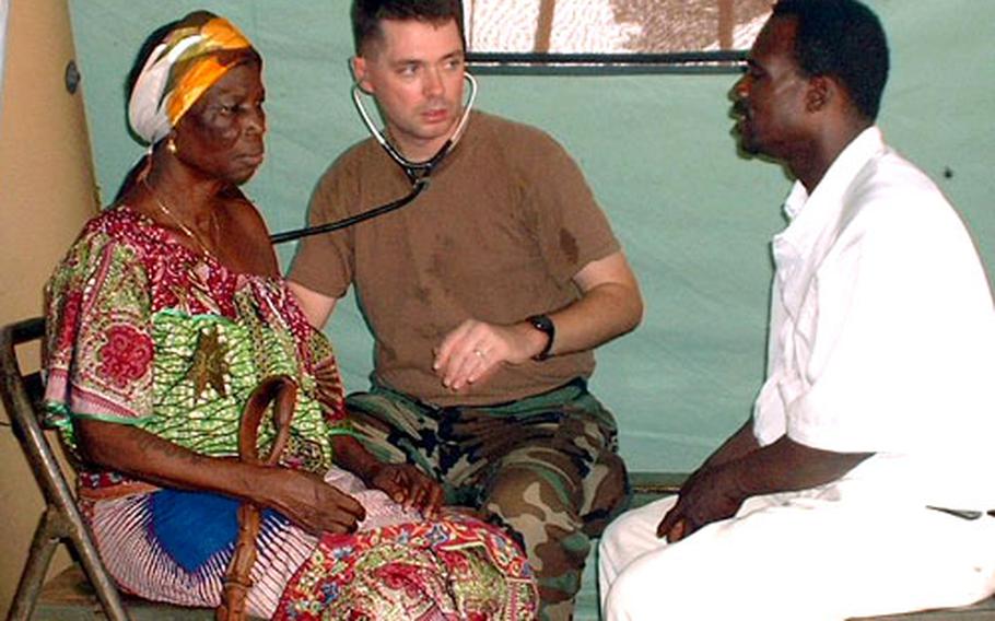 Lt. Cmdr. Mark Flynn, a family practice doctor stationed at Naval Hospital Rota, Spain, works with a translator to help a Beninese patient in Benin, Africa, this month. Seven military personnel from Rota and Stuttgart, Germany, participated in the French-led Recamp IV exercise in West Africa. Flynn said there was a widespread belief among the Beninese that the doctors could “work magic for them.”