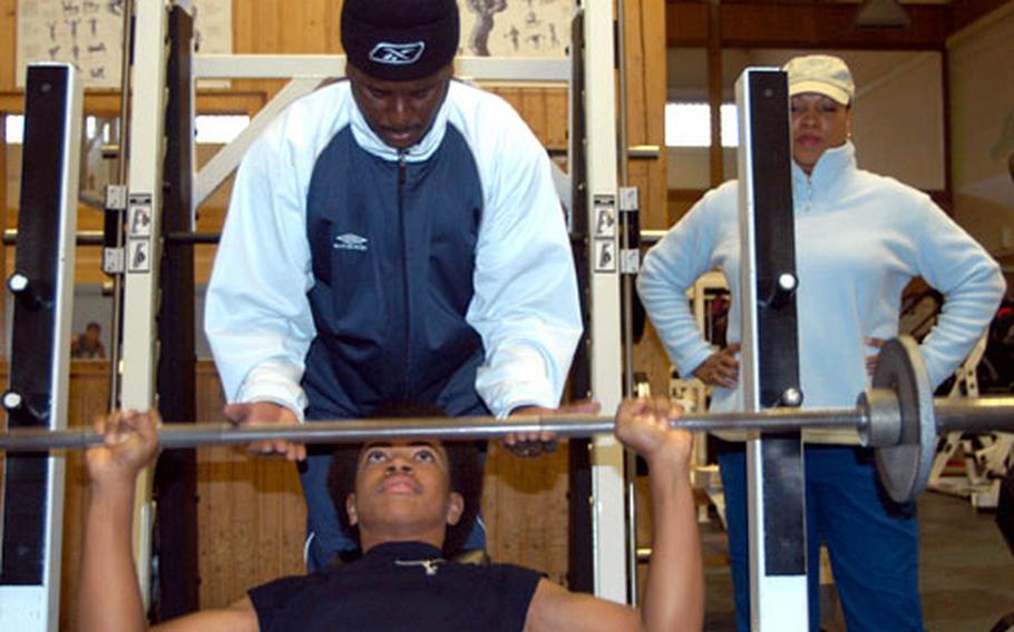 Alex Keeton, 12, bench-presses free weights while his father, Staff Sgt. David Thomas, spots him and mother Ruby Thomas watches Wednesday in Bamberg, Germany. A new Warner Barracks program allows children 12 to 16 to be certified through Child and Youth Services to use the gym without a parent present, but the Thomases still make it a family affair.