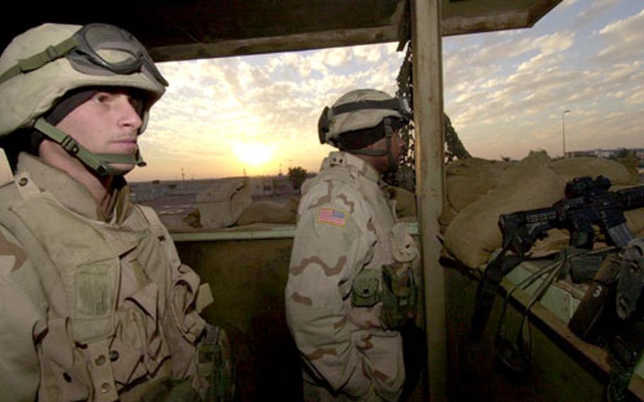 Spc. John Basco, left, and Pfc. Ronald Boudreaux, of Battery B, 1st Battalion, 141st Field Artillery Regiment, man a watchtower as the sun sets behind Camp Liberty, outside of Baghdad.