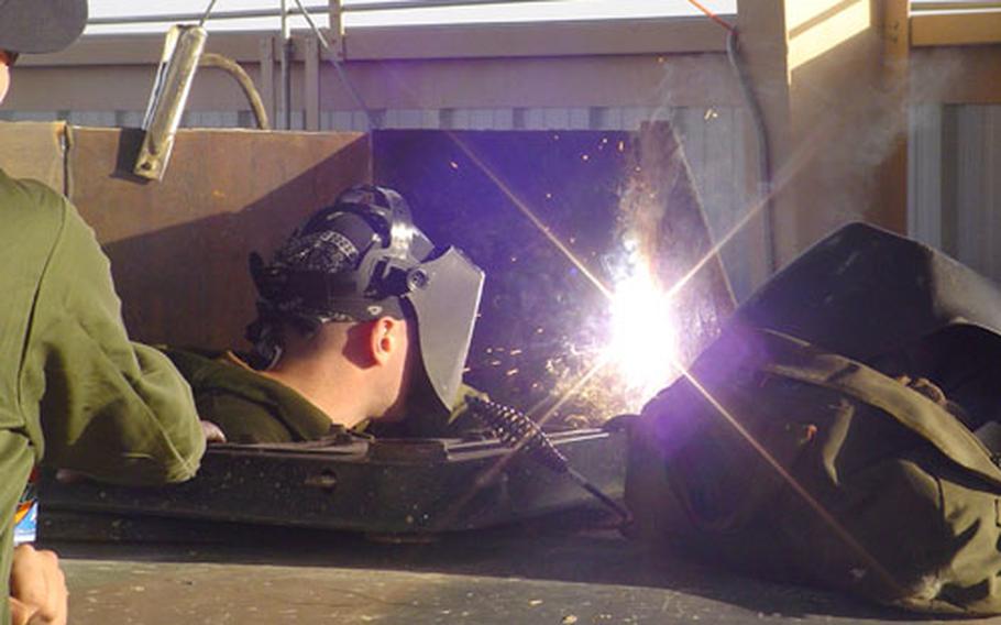 Petty Officer 3rd Class Michael Croft, a damage controlman, welds an armor plate onto the turret of an Army vehicle at Camp Buehring, Kuwait, where 15 sailors are using their Navy skills to help protect troops on missions in Iraq.