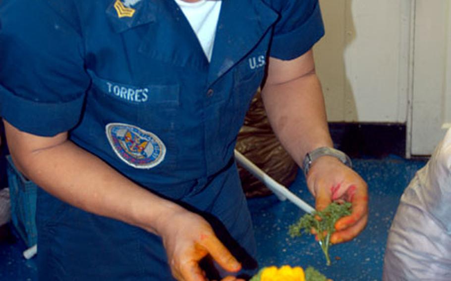 Petty Officer 1st Class Arnaldo Torres prepares table centerpieces for a semi-formal reception aboard the USS Emory S. Land off the coast of Gabon.