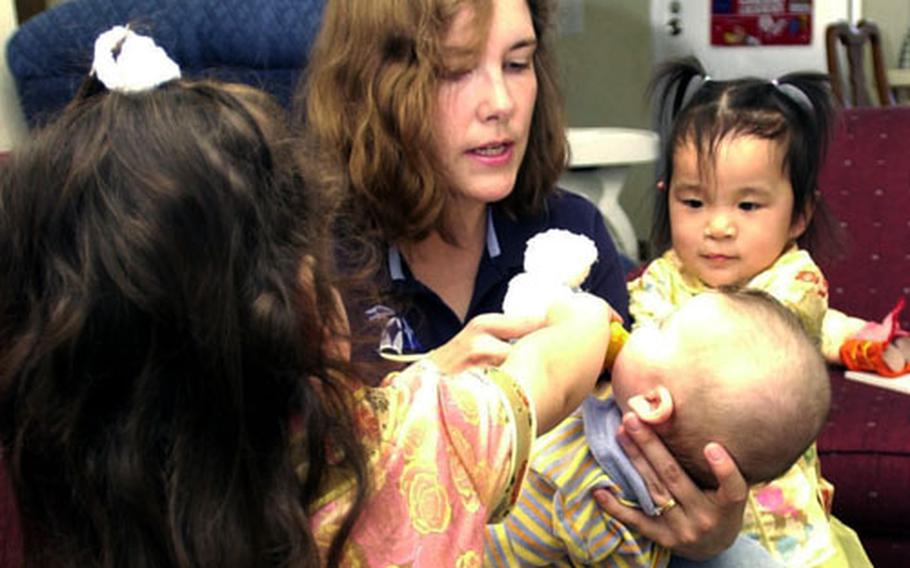 Tammy Carsten holds her 5-month-old son, Aaron, while 2-year-old daughter Amanda, left, and adopted daughter Elaina, also 2, play with him at their home on Camp Lester. Tammy and her husband, Maj. Mike Carsten, adopted Elaina from China, with help from the Okinawa adoption support group.
