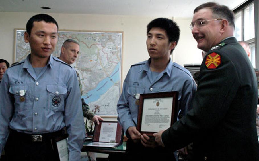 Cpl. Kim Bo-hyun, left, and Pfc. Kim Hoon pose with Area II commander Col. Timothy McNulty during a ceremony Thursday in Seoul. The two young officers were honored for pulling the husband of a U.S. officer from a burning car.