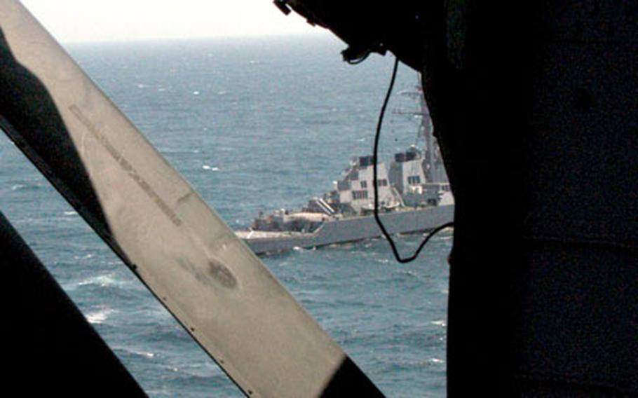 Army Spc. Paul Bates, a crew chief with the 78th Aviation Battalion at Camp Zama, Japan, leans out a window to view the USS Curtis Wilbur, during deck landing qualification training Thursday.