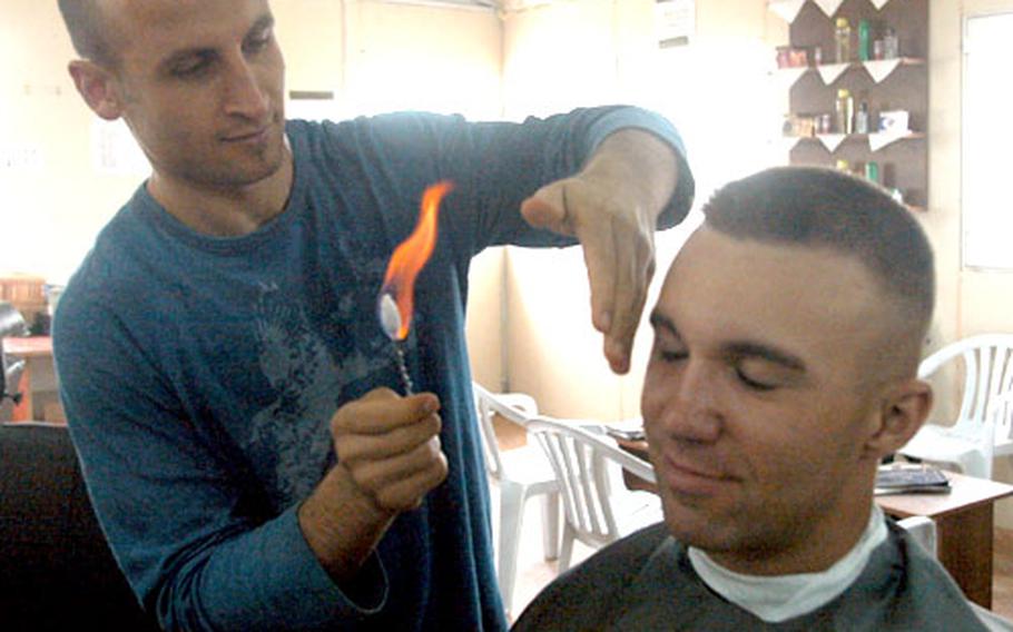 Lance Cpl. Athanasios Genos, 22, a combat correspondent for the 2nd Marine Division out of Camp Lejeune, N.C., takes a break for a haircut and massage at the Turkish-run Marine Express barber at Camp Fallujah, Iraq. Part of the Arab barber experience is the use of a flaming cotton swab to burn off ear and neck hairs.