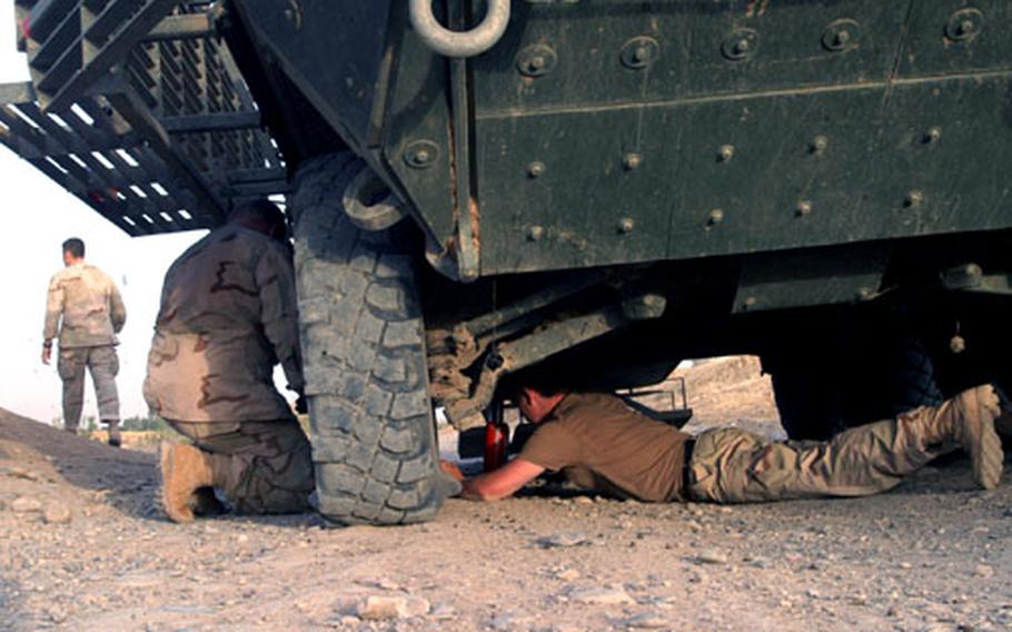Soldiers from Delta/52 Infantry Company crawl under a Stryker to change a flat tire the vehicle sustained during a recent mission. It took more than an hour to remove the flattened front tire and replace it with the one right behind it.