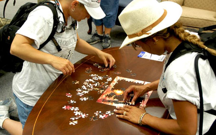 Kat Genetti, left, and Nicole Adelman put together a jigsaw puzzle at the Army and Air Force Exchange Service Mini-Mall at Aviano Air Base, Italy, on Friday. They were the first to complete the puzzle and the only ones to make it on a shuttle bus that put them way ahead in the game, a version of “The Amazing Race.”