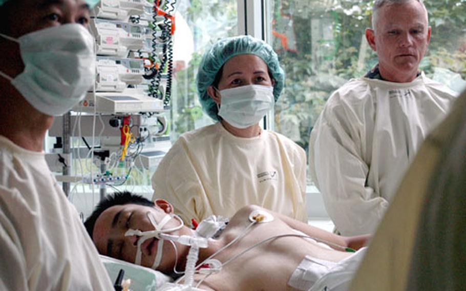 Elizabeth Lien Chu, center, and David Kim Wong, left, stand over their son, Sgt. Chang Wong of the 1st Squadron, 11th Armored Cavalry Regiment, while the recovering soldier receives a special grant of American citizenship Monday at a university hospital in Regensburg, Germany. Wong was sent to the hospital because its staff includes the foremost authorities in a new "external lung" that kept him alive after being wounded by a roadside bomb in Iraq. Col. Mike Davis, right, a former commander of Wong's unit, looks on during the ceremony.