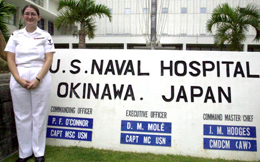 Petty Officer 3rd Class Claire Gwaltney, who works in the U.S. Naval Hospital Okinawa's Dermatology Clinic, stands at the sign outside the hospital much like her grandmother posed for a photo at an aid station there in 1945.