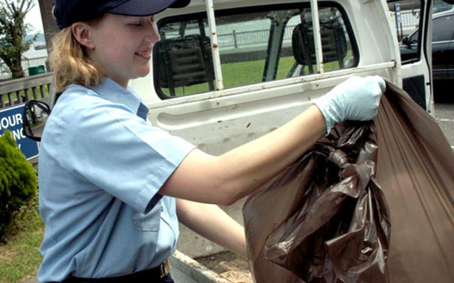 Petty Officer 3rd Class Coral Laster, a damage controlman with the Fleet and Family Support Center, loads trash bags into a truck during her rotation with the Commander Fleet Activities Yokosuka duty section.