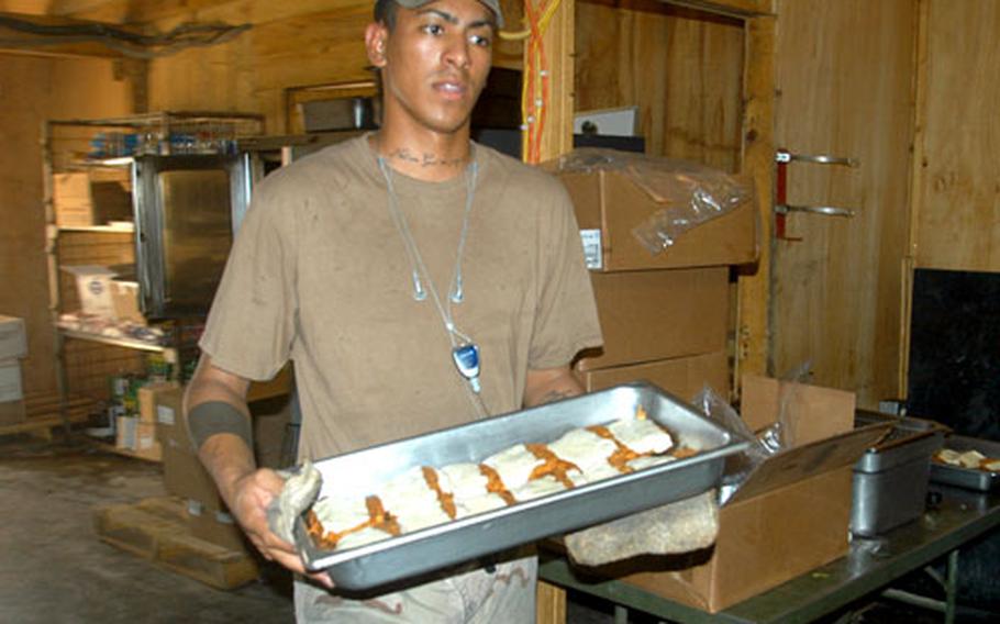 Spc. Robert Dominguez carries a tray of chicken Parmesan from one of the ovens Saturday at Forward Operation Base Lagman near Qalat, Afghanistan.