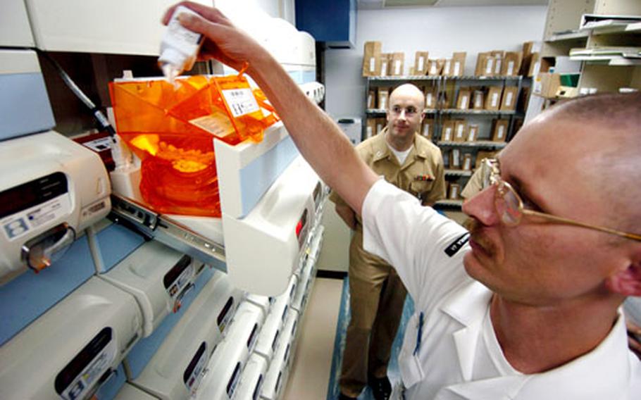 Lt. Ben Schwartz watches 2nd Class Petty Officer Scott Curry refill the Mckesson Pharmacy 2000.