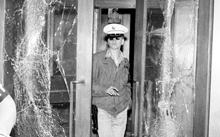 An Army officer was killed and 13 persons injured when bombs went off at V Corps headquarters in Frankfurt, Germany on May 11, 1972. A military policeman stands between the shattered glass doors at the entrance of the headquarters building.