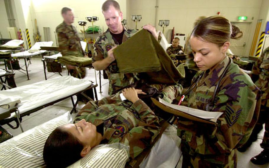 Tech. Sgt. Jeff McGaffin places a blanket over Airman Blanca Gama while Tech. Sgt. Courtney Davis looks over Gsma’s medical records during a training exercise Friday at Yokota Air Base, Japan.