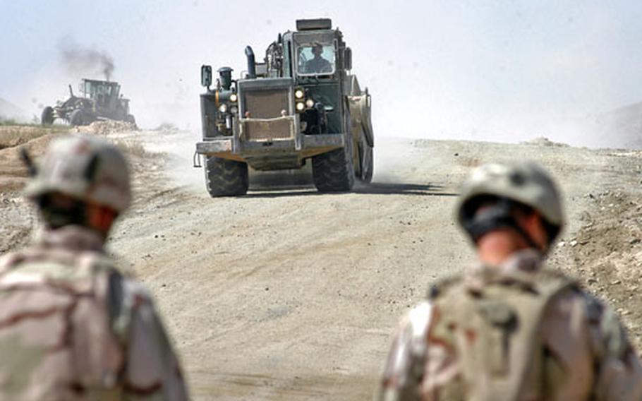 Soldiers from Task Force Pacemaker walk down the shoulder of the Kandahar-to-Tirin Kot road as construction equipment operates in the background. Since April, about 1,000 U.S. soldiers from the task force have been working on the last 48 miles of the 76-mile road. The road has been under construction since June 2004.