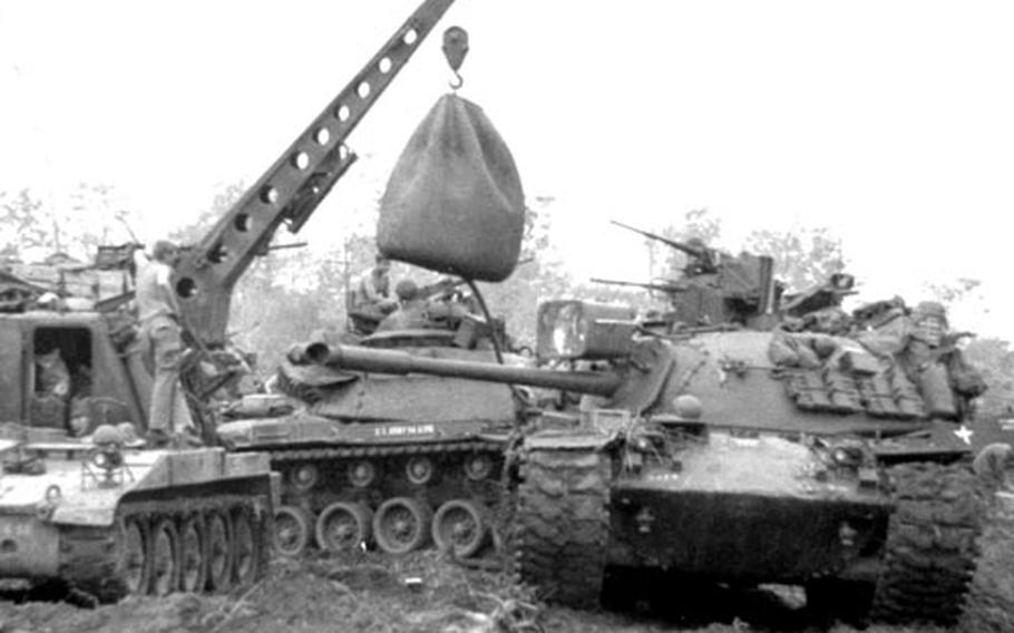 Armored vehicles are refueled from a fuel bladder lifted by a light tracked vehicle recovery unit.