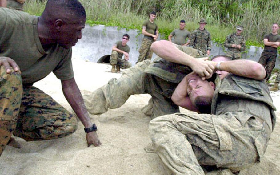 Staff Sgt. Antonio Mitchell, left, watches as Lance Cpl. Roberto Soares get choked by Lance Cpl. Sean Wilkinson during a grappling training session involving military policeman on the beach of Camp Schwab Tuesday.