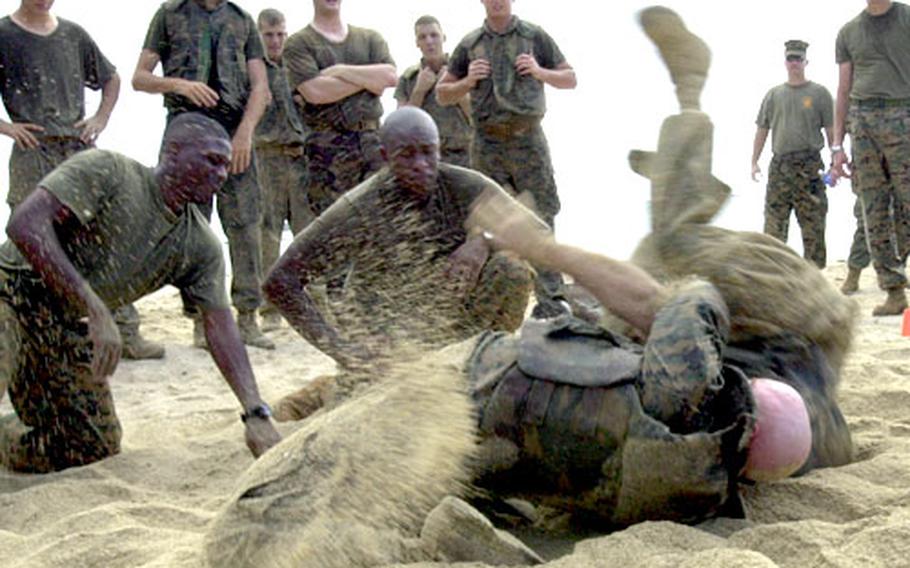 A Marine military policeman flips his opponent as fellow Marines look on during a grappling training session on the beach of Camp Schwab.