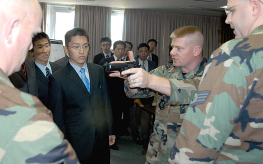 Staff Sgt. Nickolas Cordatos, center, demonstrates the features of a 9 mm handgun for Japanese National Police cadets Monday morning at 35th Security Forces Squadron headquarters at Misawa Air Base.