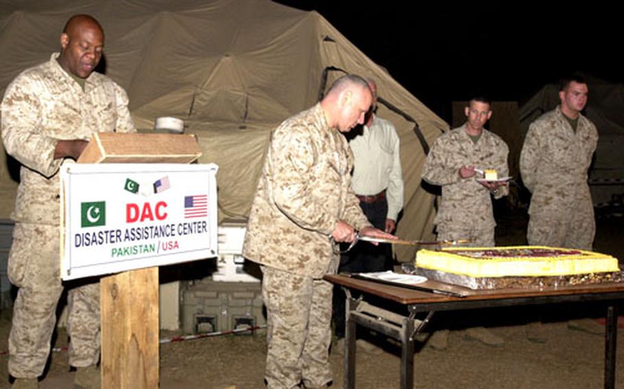Maj. Grover Wright, camp commandant for the Disaster Assistance Center on Chaklala Air Field, Pakistan, reads about the significance of the cake-cutting ceremony while Col. Mark Losack, deputy commander of the DAC, uses a sword to do the honors Thursday during a celebration of the Marine Corps’ 230th birthday.